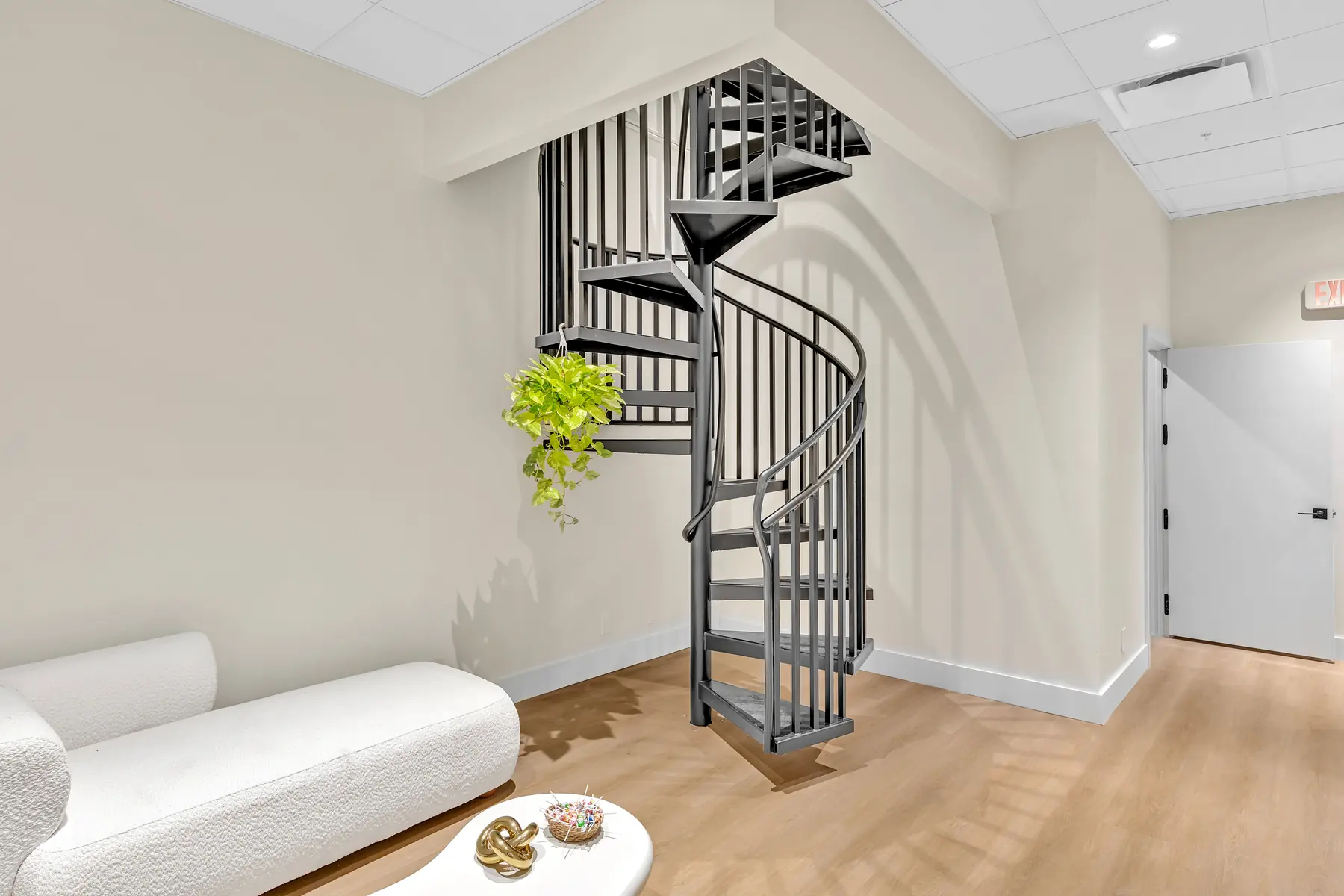 Lobby with spiral staircase, hanging plant and white bouclé lounge