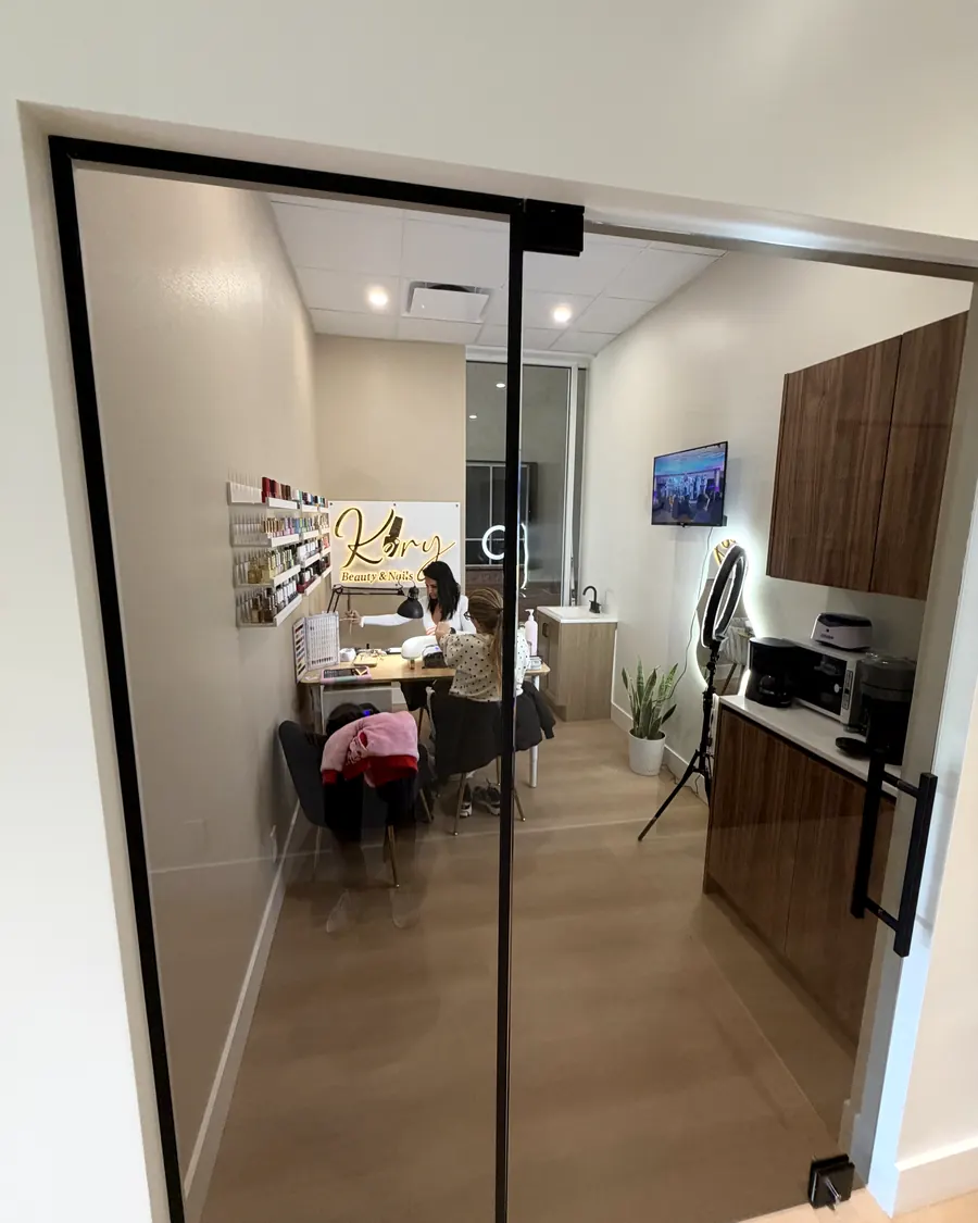 Beauty suite behind a glass door, with a pro working with a client, product shelves and a ring light